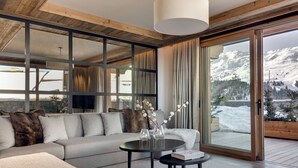 Una sala de estar moderna con un amplio sofá seccional, una mesa redonda y vistas a un paisaje montañoso nevado a través de ventanas de techo a suelo.