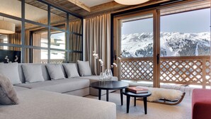 Una sala de estar moderna con un amplio sofá modular, una mesa redonda de centro y vistas a un paisaje montañoso nevado a través de grandes ventanales.