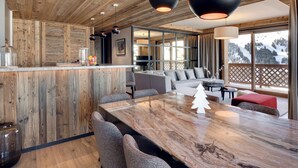 Un interior moderno con techo de madera, una zona de comedor con mesa de mármol y vistas a una montaña nevada.