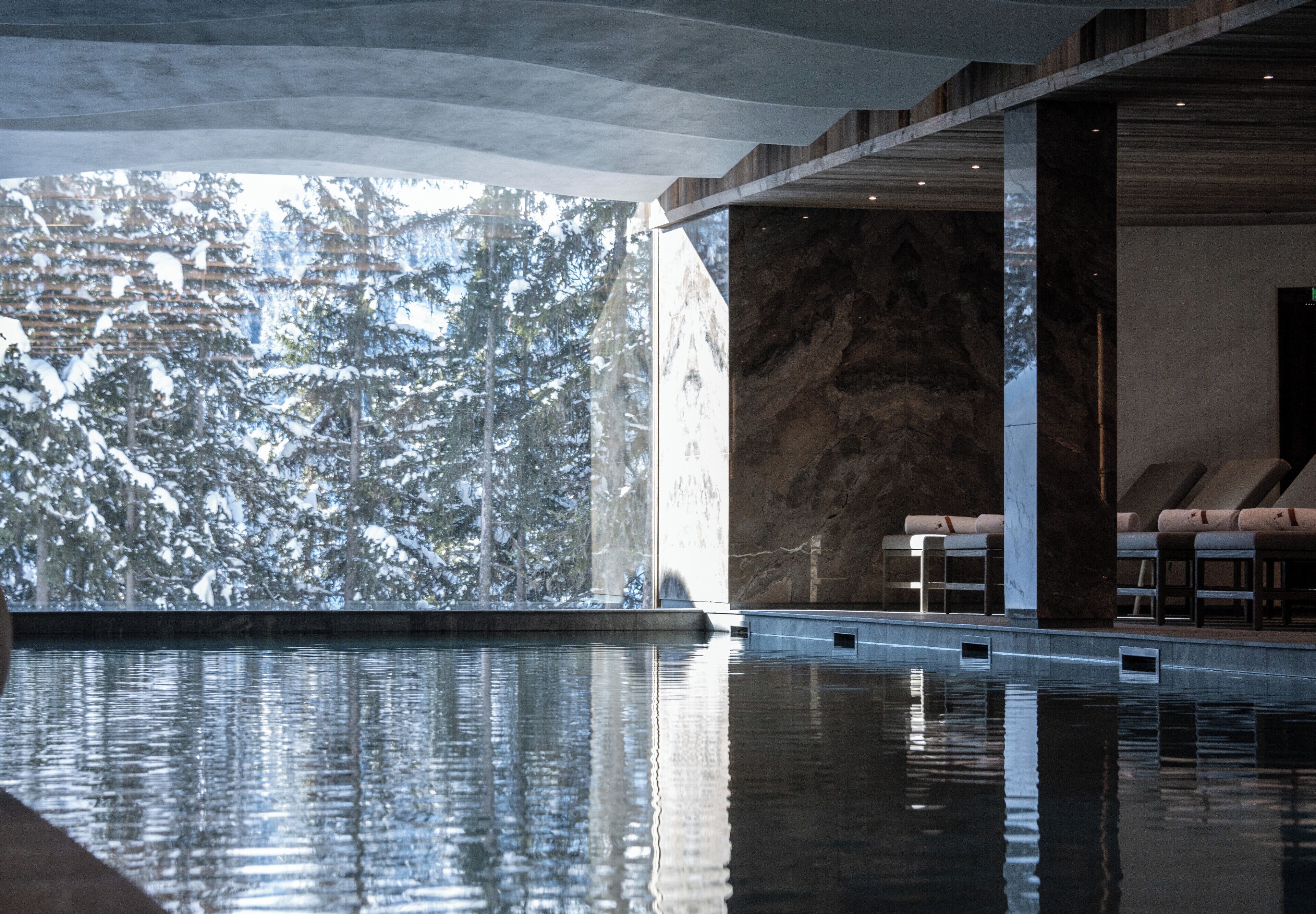 A modern indoor pool with a clear view of snow-covered trees outside.