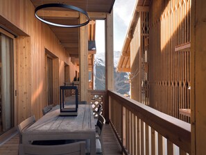 A wooden corridor with a bench and a table, leading to a balcony with a view of mountains.