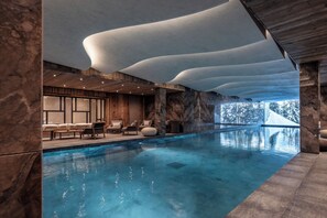 Une piscine intérieure moderne avec une vue dégagée sur l’extérieur, des panneaux de bois et des espaces aménagés pour se détendre.