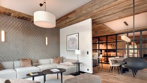 Una sala moderna con un sofá modular, una mesa de centro redonda y un otomán grande. Se ve un área de comedor con una mesa y sillas a través de una pared abierta.