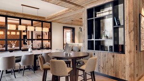 A modern dining area with a round table, bar stools, and a large wooden bookshelf.