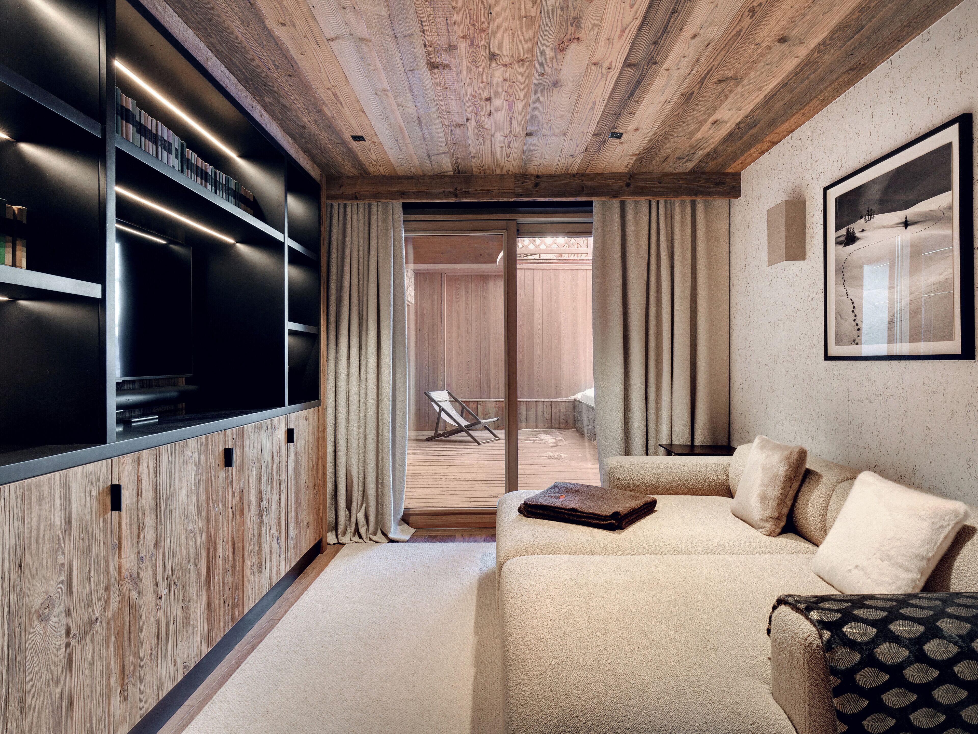 A modern living room with a wooden ceiling, a large flat-screen TV, a beige sofa, and a framed picture on the wall.