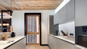 A modern kitchen with light wood flooring, grey cabinets, and a wooden-framed window.