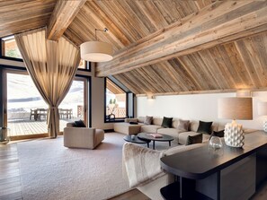 Una sala de estar moderna con techo de madera, ventanas amplias, un conjunto de sofás y una mesa de centro.