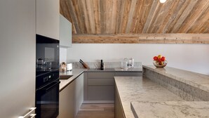 A modern kitchen with a wooden ceiling, a built-in oven, and a marble countertop.