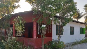 A building with a red exterior, a white wall, and green shutters. There is a tree with white flowers in front of the building. - Jambiani Holiday House (Jambiani)