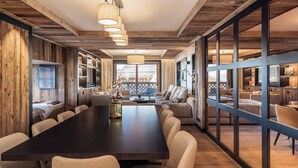 A spacious dining area with a long table and multiple chairs, wooden walls, and large windows offering views.