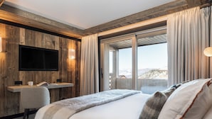 A modern bedroom with a large bed, a desk, and a TV mounted on a wooden wall.