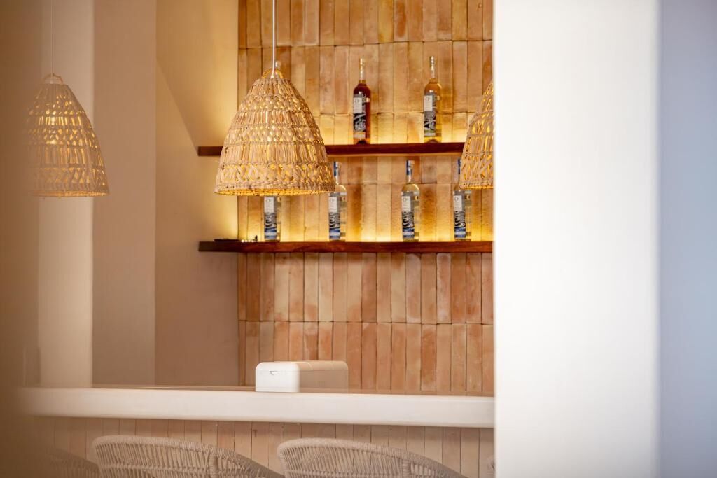 A bar area with hanging lamps, shelves with bottles, and wicker chairs.