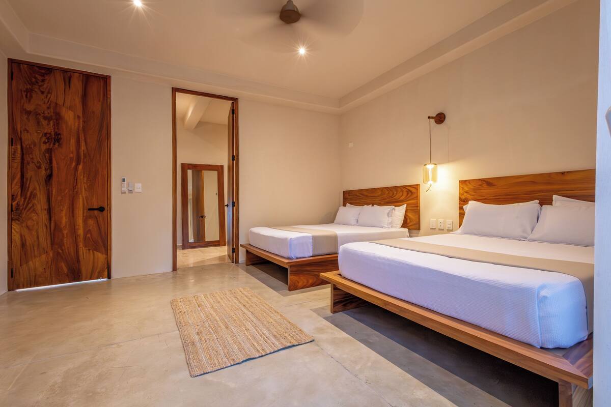 A hotel room with two beds, a wooden door, a mirror, and a light fixture.