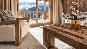 Una habitación acogedora con techo de madera, un sofá, una cama y vistas a un paisaje nevado a través de un ventanal.