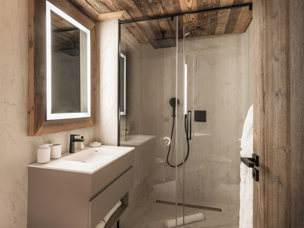 Un baño moderno con cabina de ducha de vidrio, techo de madera y un espejo grande sobre el lavabo.
