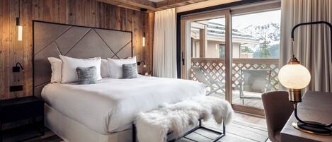 Un dormitorio moderno con una cama grande, paneles de madera, un balcón con vistas a las montañas y una mesita de noche con una lámpara.