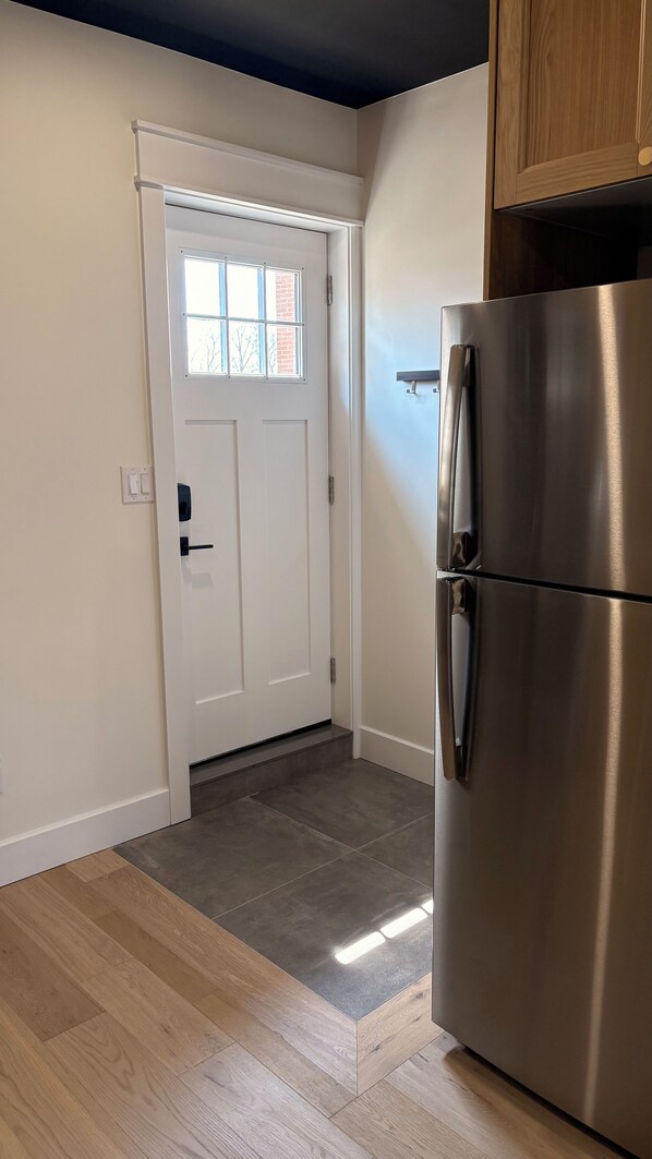 A kitchen with a stainless steel refrigerator, a white door with a window, and a wooden cabinet above it.