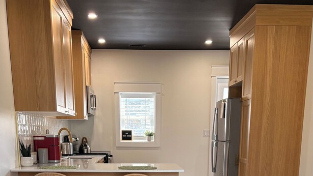 A modern kitchen with wooden cabinets, a central island with stools, a refrigerator, and a window with blinds.