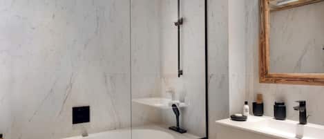 Un baño moderno con pared de mármol, tocador de madera, un espejo grande y cabina de ducha con mampara de vidrio.
