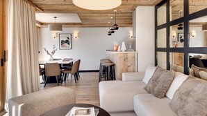 En moderne stue med træloft, en stor sofa, et sofabord og et spiseområde i baggrunden.