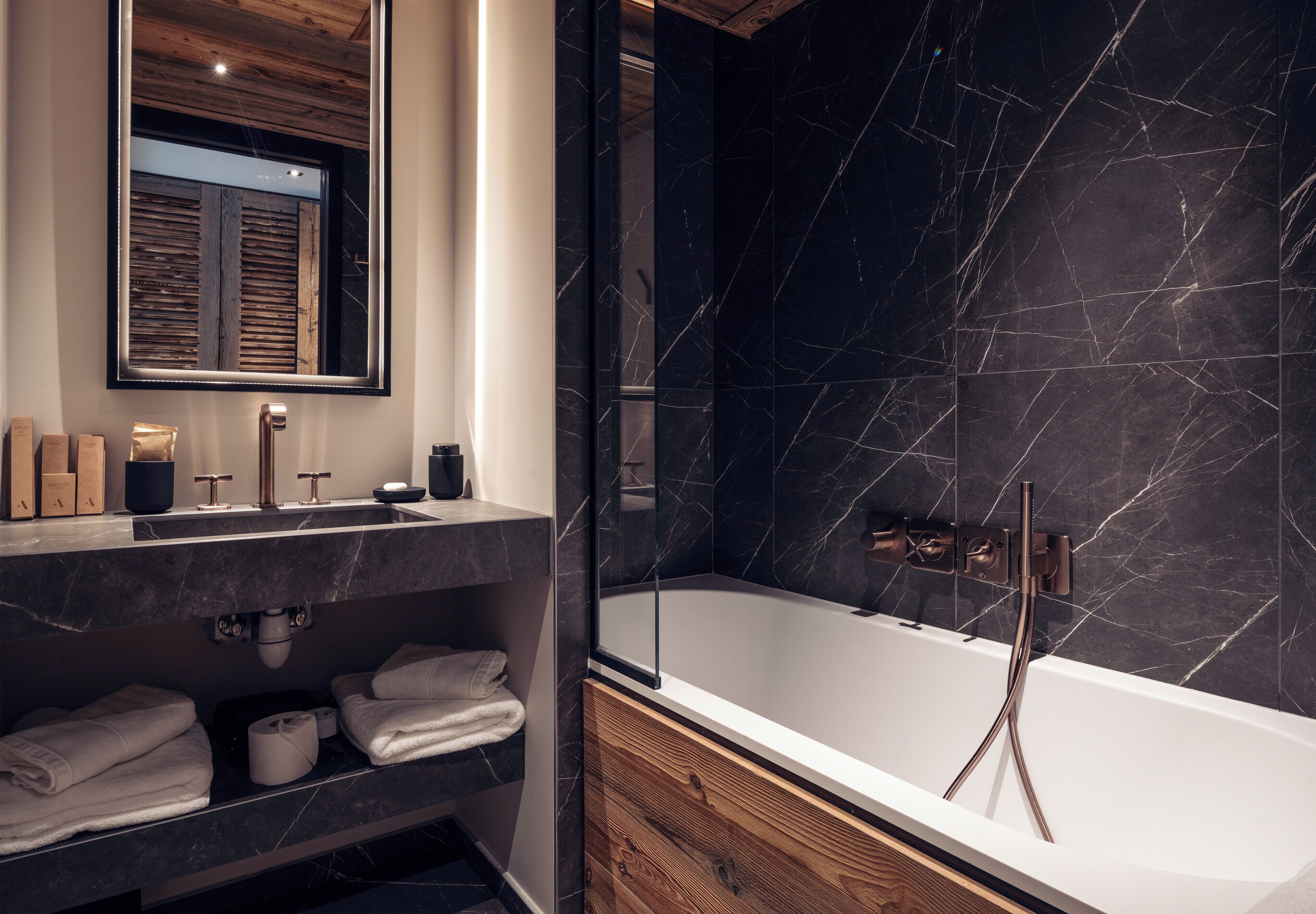 Un baño moderno con lavamanos de mármol, tocador de madera y bañera independiente.