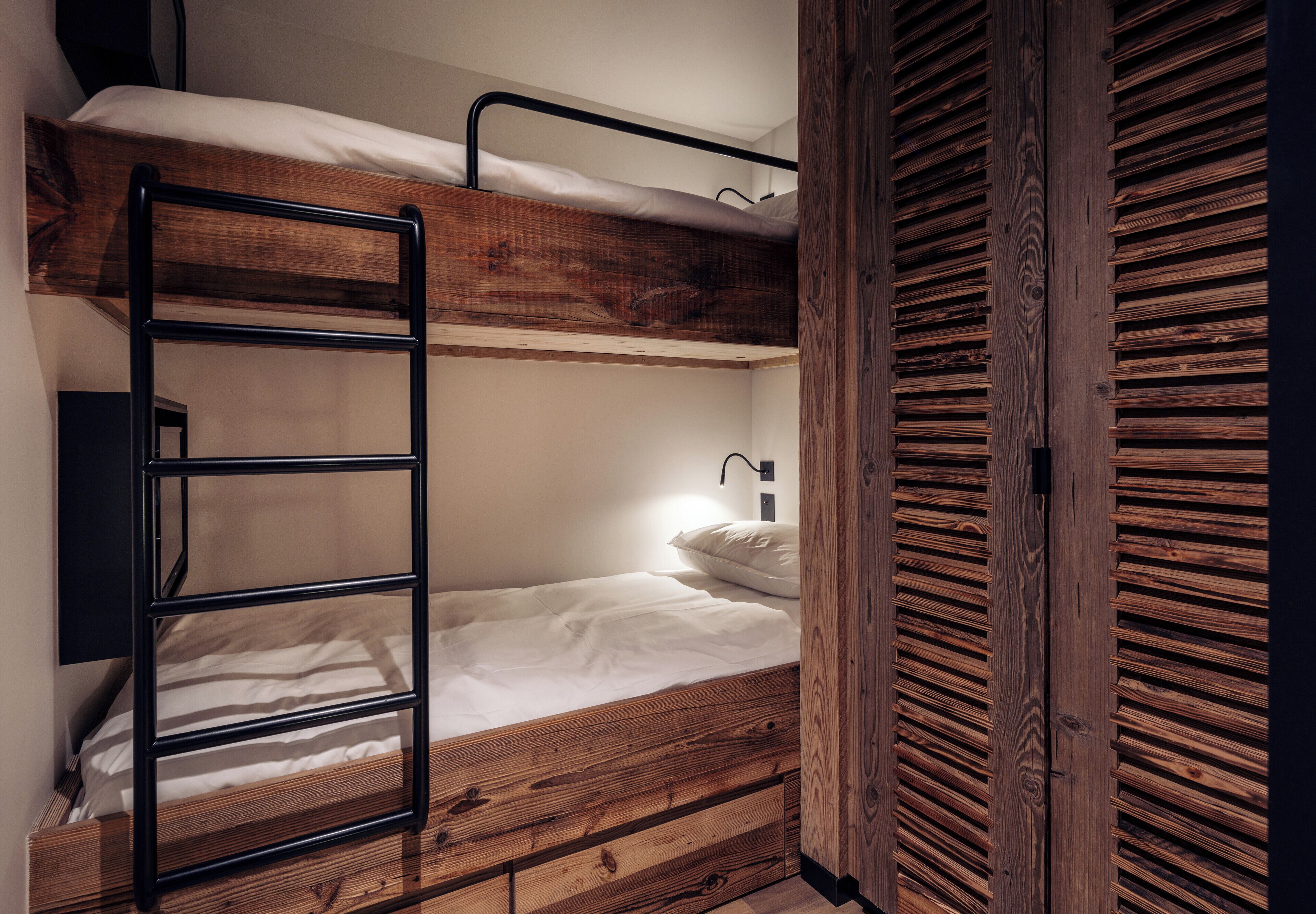 Una cama litera con escalera, cabecero de madera y una lámpara de noche.