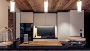 A modern kitchen with a wooden ceiling, three pendant lights, a black stove, and a wooden cutting board.