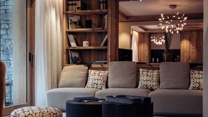 A cozy living room with a sofa, ottoman, and a bookshelf filled with books and decorative items.