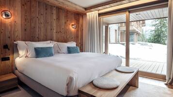 A modern bedroom with a wooden wall, a large bed with pillows, a bedside table, and a view of a snowy landscape through a glass door.
