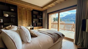 A bedroom with a large bed, wooden walls, a built-in shelf, and a balcony with a mountain view.