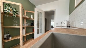 A kitchen with wooden shelves, a countertop, and a door leading to another room. - Cozy, bright vacation apartment in trendy boho style #Cosiness Company (Cuxhaven)