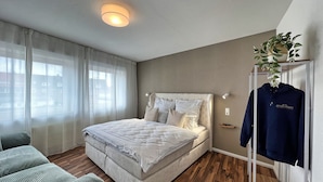 A bedroom with a bed, a bedside table, a hanging plant, and a coat rack. - Cozy, bright vacation apartment in trendy boho style #Cosiness Company (Cuxhaven)