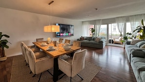 A modern living room with a dining area, a sofa, and a TV mounted on the wall. - Cozy, bright vacation apartment in trendy boho style #Cosiness Company (Cuxhaven)