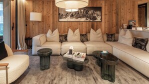 A cozy living room with a sofa, coffee table, and side tables, featuring wooden paneling and a mountain painting.