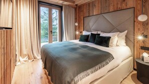 A bedroom with a large bed, wooden paneling, a window with curtains, and a bedside table with a lamp.