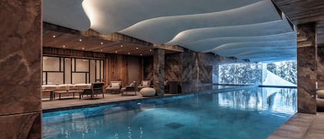 Una piscina interior moderna con vista despejada al exterior, paneles de madera y zonas de estar.