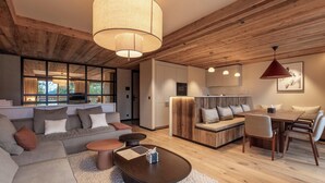 Una sala de estar moderna con un sofá grande, una mesa de centro y un comedor con sillas. El techo es de madera y hay un ventanal amplio que proporciona luz natural.
