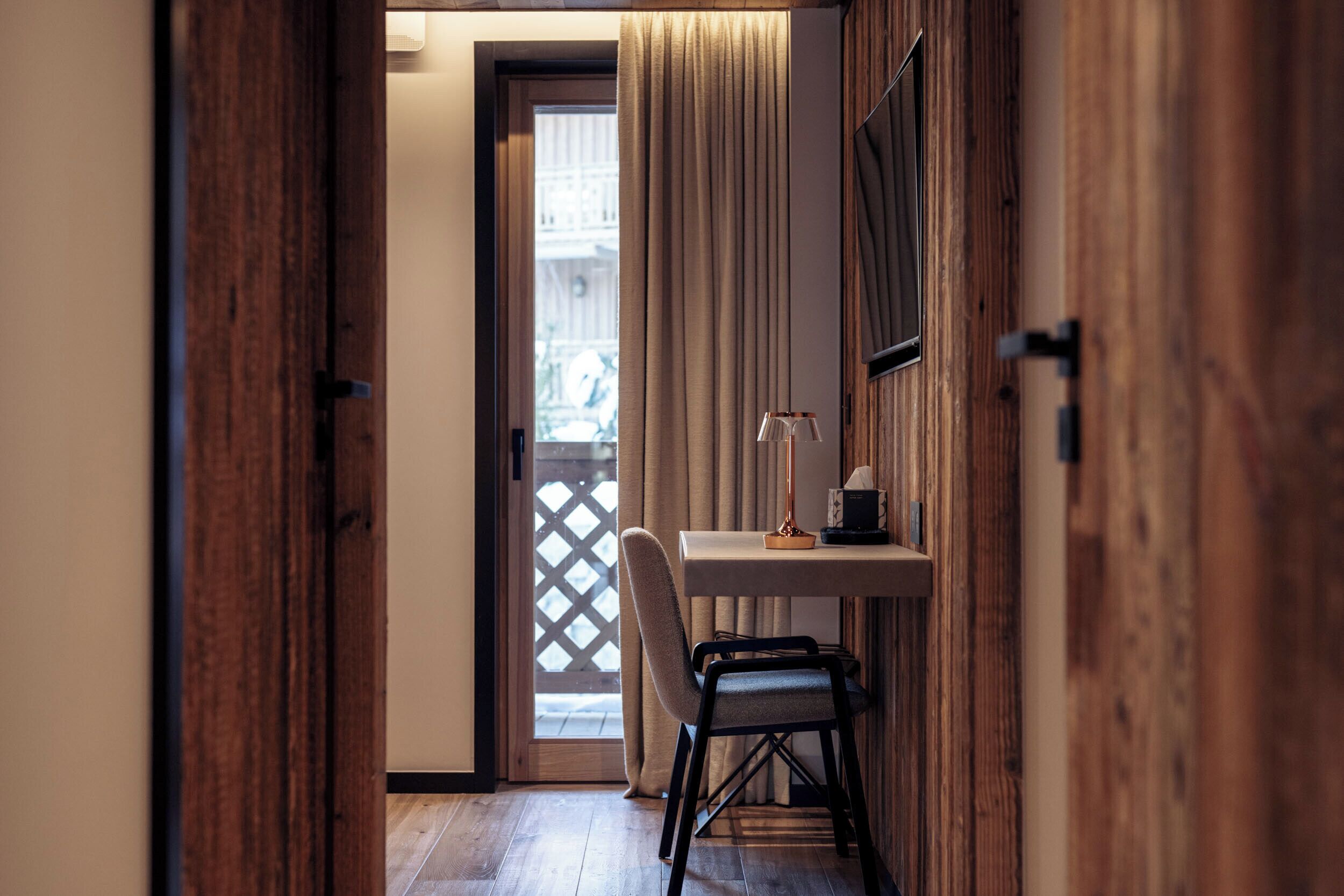 A hallway with a wooden door, a desk with a chair, and a window with curtains.