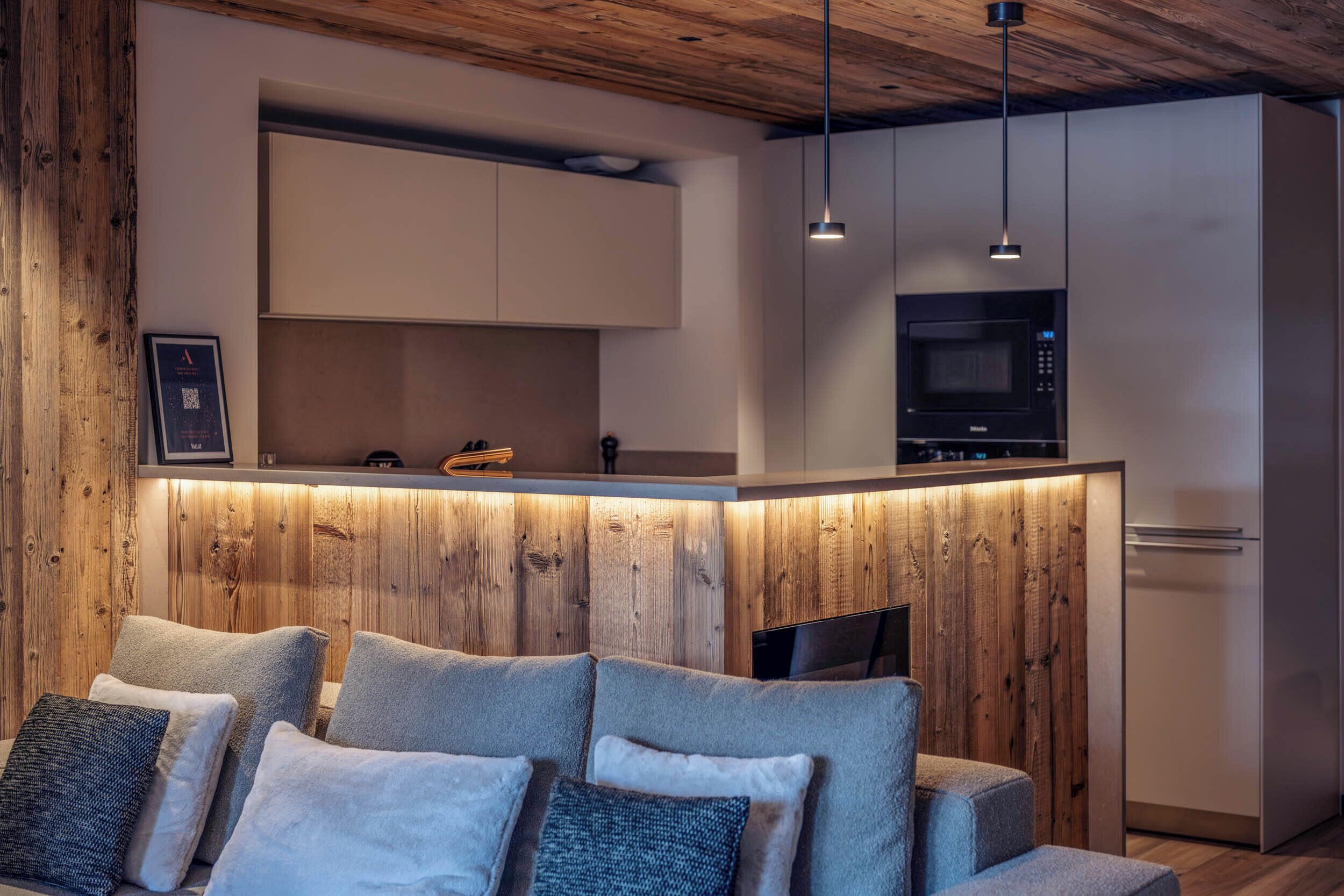 A modern kitchen with a wooden accent wall, a built-in microwave, and a white refrigerator.