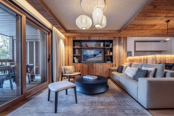 A modern living room with a large TV, wooden panel walls, a round coffee table, and a sofa. - Antarès URSA 203 -   luxury apartment ski in/ski out (Les Allues)