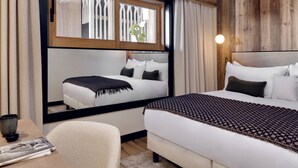 Una habitación de hotel con una cama grande, una cama más pequeña, un escritorio con una silla y una ventana con cortinas.