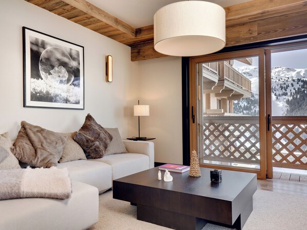 A modern living room with a sofa, a coffee table, and a large window with a view of snowy mountains.