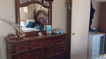 A bedroom with a wooden dresser, a bed with patterned bedding, a mirror, and a deer head decoration.