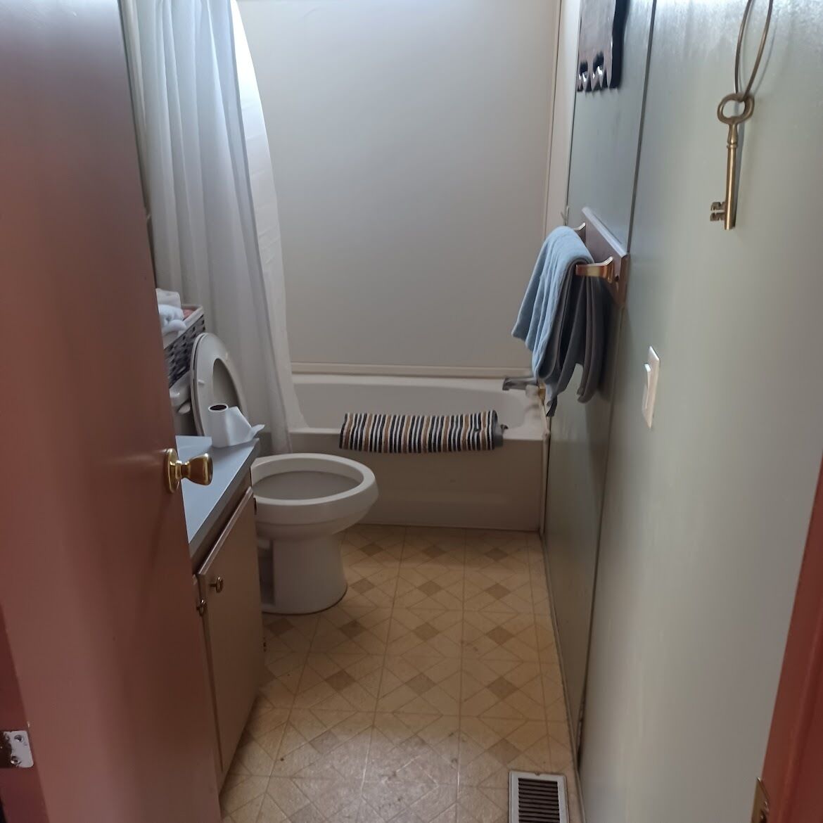 Une petite salle de bain comprenant des toilettes, une baignoire et une douche. On y trouve un porte-serviettes sur lequel sont suspendues des serviettes.