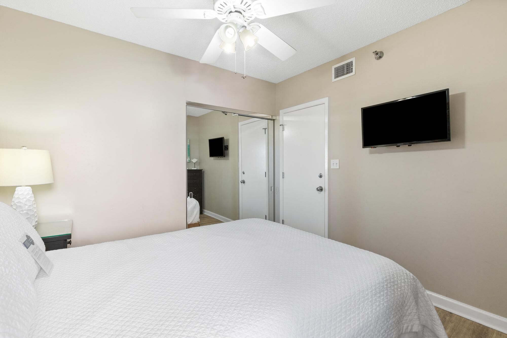 A hotel room with a bed, a ceiling fan, a TV, and a door leading to a bathroom.