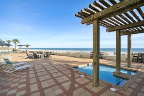 Área de piscina com espreguiçadeiras e um pergolado com vista para a praia.