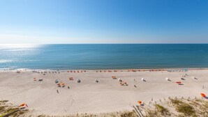 A wide beach with numerous umbrellas and beach chairs, a clear sky, and calm sea. - Shoalwater 1202 (Orange Beach)