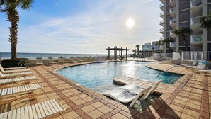 A pool area with lounge chairs, a palm tree, and a view of the ocean. - Shoalwater 1202 (Orange Beach)
