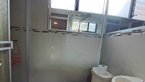 A bathroom with a toilet, bidet, and sink. There is a glass shower enclosure and a window above the toilet.