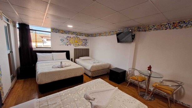 A hotel room with two beds, a TV, a small table with chairs, and a window with curtains.
